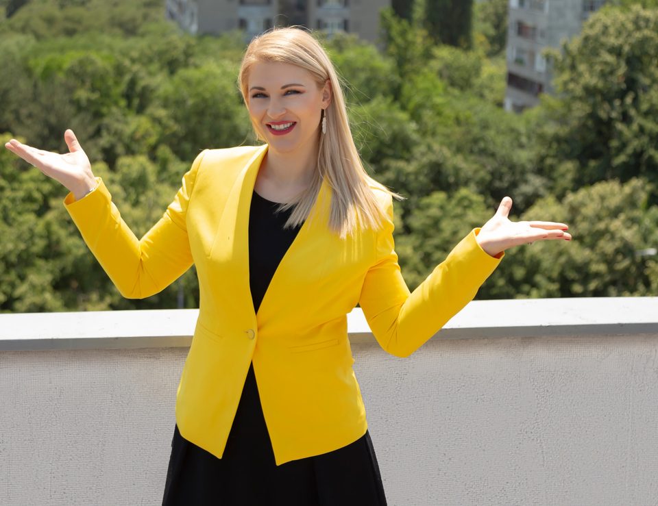 Dr. Zorana Pravdić im gelben Blazer breitet im Freien lachend die Arme aus